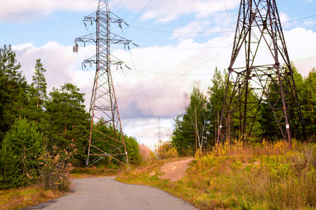 Autumn landscape, road, forest. Metal support for high voltage power lines against the sky. Power...