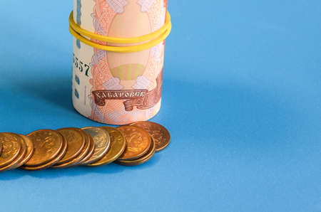 Russian rubles rolled into a tube and metal coins on a blue background. World economic crisis. Cash...