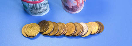 Russian paper rubles rolled up in a grocery cart on a blue background. Metal coins. World economic...