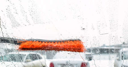 The brush cleans the wet glass of the car from snow and water. Water drops on blurred glass. Selective focus.の写真素材