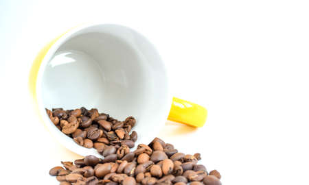 Coffee beans scattered from yellow ceramic cup isolated on white background. Copy space for text. Selective focus.の写真素材