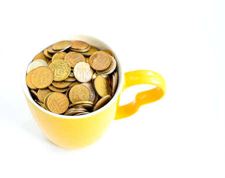 Ceramic cup filled to the top with metal coins isolated on white background. Store personal savings. Selective focus. Copy space for text.の写真素材