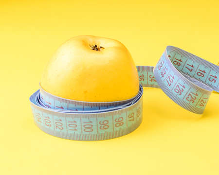 A yellow apple wrapped in a centimeter tape