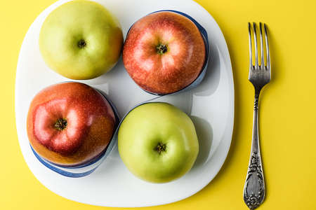 Red and yellow apples, wrapped with a centimeter tape on a white plate, on a yellow background, next...