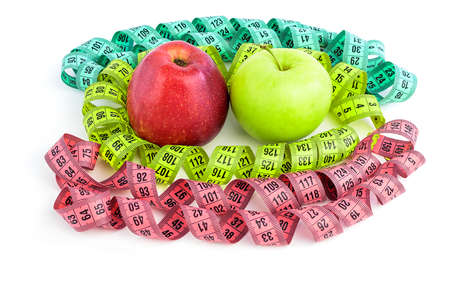 Bright colored measuring tapes, twisted in a spiral around a red and green apple, isolated on a...