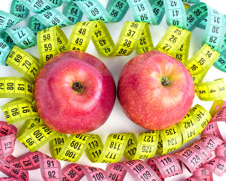 Two red apples and a centimeter tape isolated on a white background. Bright colored measuring tapes, twisted in a spiral around apples. Healthy and proper nutrition, calorie content. Fitness, diet, weight loss concept.の写真素材