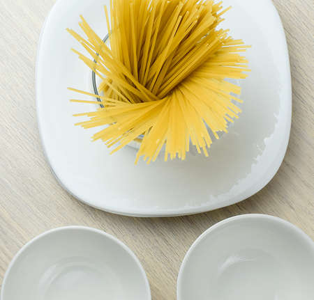 White clean ceramic plates, raw pasta in a glass jar on the kitchen table. Copy space. Top view.の写真素材