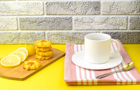 White cup of tea with a saucer on a kitchen napkin, homemade cookies, sliced fresh lemon on a wooden...