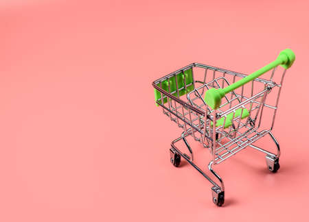 Empty miniature supermarket trolley on a colored background. The concept of buying and selling goods. Online sales on the Internet. Selective focus, copy space.の写真素材