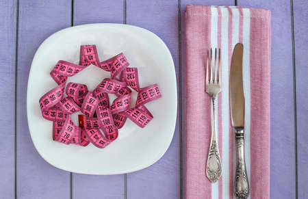 Bright measuring tape on a white plate. Fork, knife, kitchen napkin on a colored background. Concept...