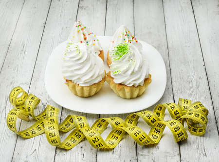 Cupcake with cream, tape measure, white plate, cotton napkin on a light wooden background. Healthy...