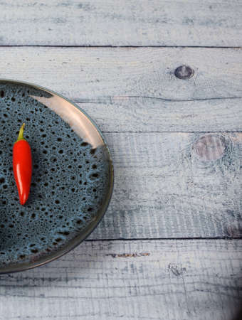 One small red chili pepper on a colored plate on a light wooden background. Flat lay. Vertical photo.の写真素材