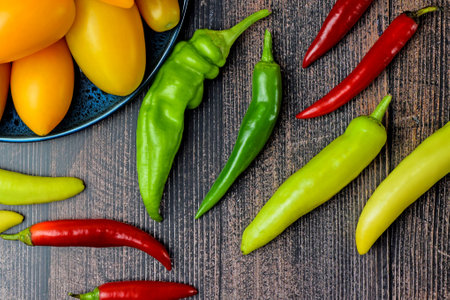 Bright colored chili peppers and fresh yellow tomatoes in a plate on a dark wooden background Harvesting. Layout of fresh vegetables. Flat lay.の写真素材