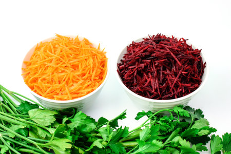 Grated carrot and grated beet in white bowls, fresh green parsley, isolated on white. Set of vegetables for cooking borscht. Selective focus. Side and top view.の写真素材