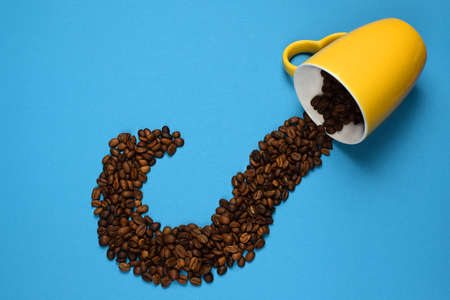 Coffee beans scattered from a yellow cup, against a blue background. Coffee beans are in the form of a question mark. Copy space for text. Flat lay, top view. Selective focus.の写真素材