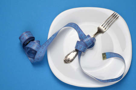 Centimeter is wound on a fork, white plate, blue background. Healthy food, calorie content. Diet,...