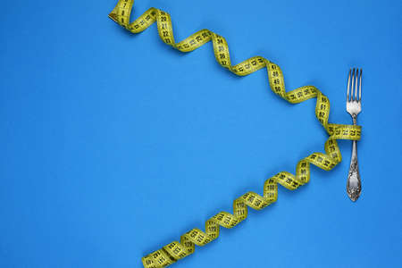 Centimeter and fork on a blue background. Healthy food, calorie content. Diet Fitness Concept. Top View. Flat Lay. Copy space for text.の写真素材