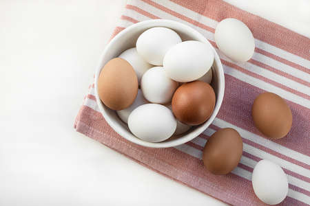 Chicken eggs in a white bowl. Ingredient for breakfast on a cotton napkin. Top view, flat lay....
