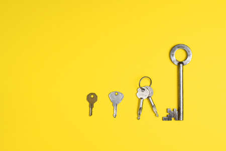 Door keys of different shapes arranged in a row against a bright yellow background. Flat lay...