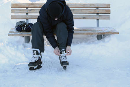 Man laces up hockey skates on an ice skating rink. Hockey gloves. Ice skating outdoors.の写真素材