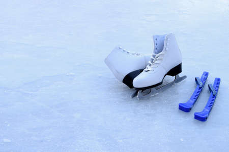 White figure skating skates with blade covers stand on an outdoor ice skating rink. The concept of winter sports and recreation.の写真素材