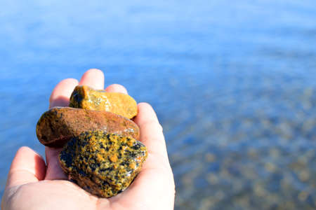 Natural sea stones in the palm of your hand against the background of sea water. Blurred background. selective focus.の写真素材
