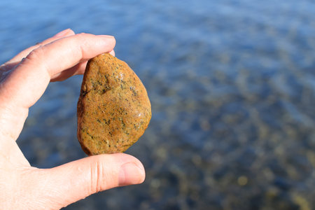 Man holds a natural stone with his fingers on the background of the sea. Blurred background.