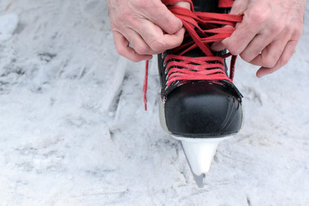 Man ties the laces of his hockey skates on an ice rink. Red laces on skates. Hockey equipment.の写真素材