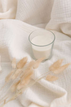 A glass of delicious fresh milk on a white fabric background. Fluffy spikelets in the corner set the direction of the imageの写真素材