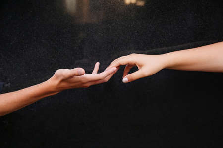A guy and a girl reach out to each other and touch their fingers on a glossy black background. A place for your advertising.の写真素材