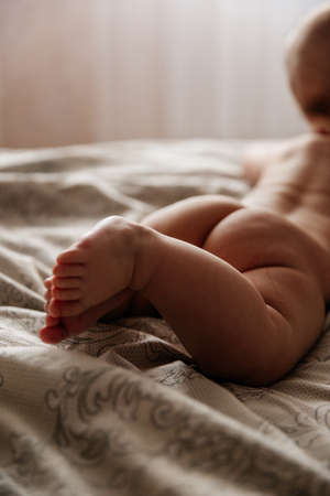 Small fingers on the chubby legs of a newborn. Cute folds all over the babys body speak about his health. The child is lying on the bed.の写真素材