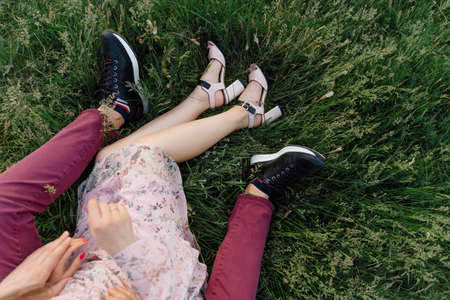 A guy in red jeans and a girl in a light summer dress are resting on the bright green grass, holding hands.の写真素材