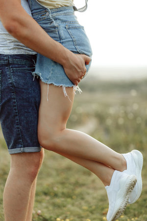 The guy holds the girl with strong hands against the background of a beautifully blurred field. She has long slender legs in white sneakers.の写真素材