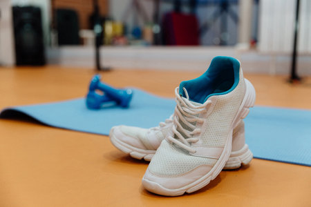 White sports sneakers with laces on the yellow floor. Next to it is a yoga mat and two small blue dumbbells. Everything you need for fitness.の写真素材