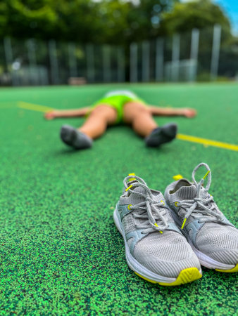 A person is lying on the ground next to a pair of stylish sneakers, which are conveniently positioned nearby them on the grassの写真素材