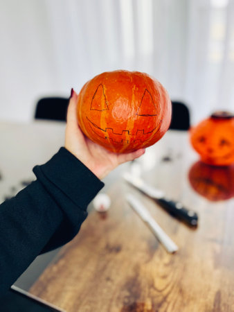 Cropped shot of female carving large orange pumpkin for Halloween party while sitting at wooden table at home, high quality photoの写真素材