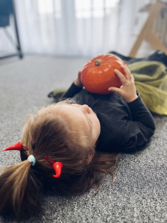 A little girl in a witch costume for Halloween is sitting at a table with sweets and pumpkins. Baby girl celebrate Halloween in a decorated room. High quality photoの写真素材