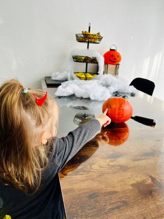 A little girl with long hair covers her eyes with her palms to a pumpkin that was made for the Halloween holiday.の写真素材