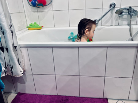 Cute adorable baby girl taking foamy bath in bathtub. Toddler playing with bath rubber toys. Beautiful child having fun with colorful gum toys and foam bubbles. High quality photoの写真素材