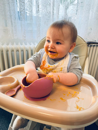 Portrait of an adorable cute baby eating with a face stained in food while in a child's dining chair..の写真素材