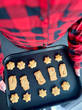 Top view of Christmas gingerbread cookies from raw dough on baking tray, ginger, cinnamon, deer shaping biscuit, freshly backed cookies on red plaid napkin over green. Winter holidays flat lay.の写真素材