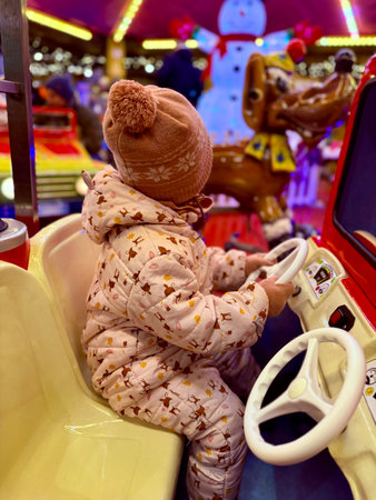 Happy little girl in warm red jacket and knitted reindeer hat riding carousel horse during family trip to traditional German Christmas market.の写真素材