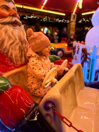 Happy little girl in warm red jacket and knitted reindeer hat riding carousel horse during family trip to traditional German Christmas market.の写真素材