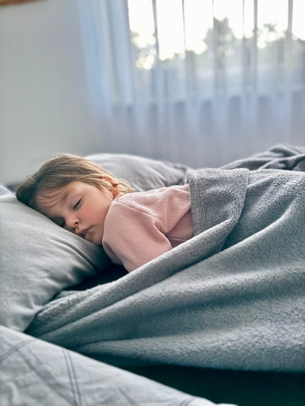 Adorable little girl is sleeping in the bed at homeの写真素材