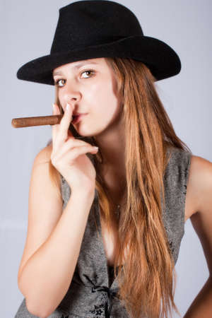 Portrait of the beautiful and stylish girl in a hat with a cigar.の写真素材