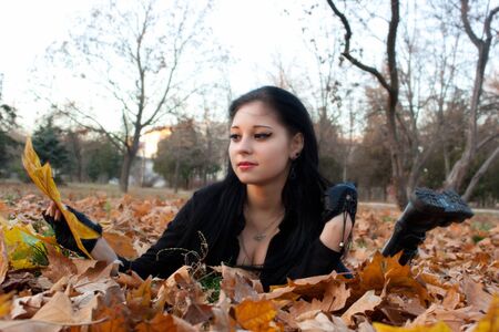 The stylish girl the teenager sits on autumn leaves.の写真素材