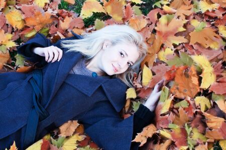 The stylish girl the teenager sits on autumn leaves.