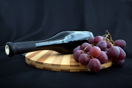 Bottle of wine and grapes lying on a board on a black backgroundの写真素材