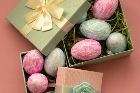 Easter concept. Bright easter eggs in gift boxes with bows on a pink stylish background
