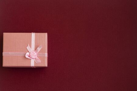 Beautiful pink gift with a bow on a burgundy texture background. Greeting card with copy space...